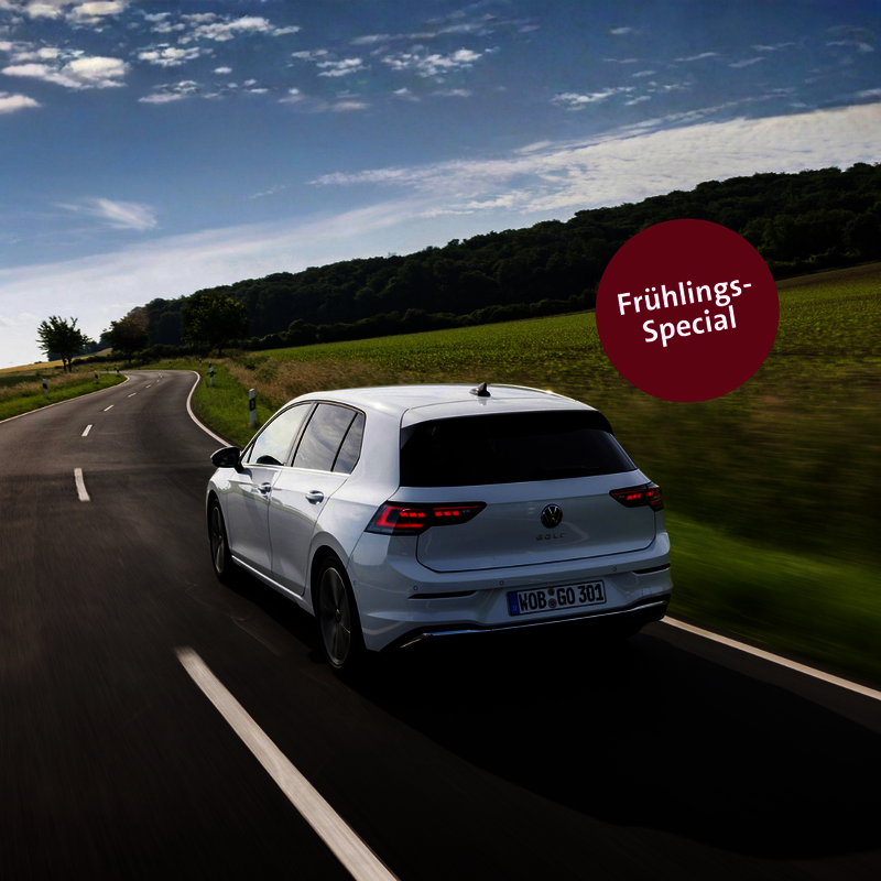 Weißer VW Golf fährt auf einer Landstraße bei Sonnenschein